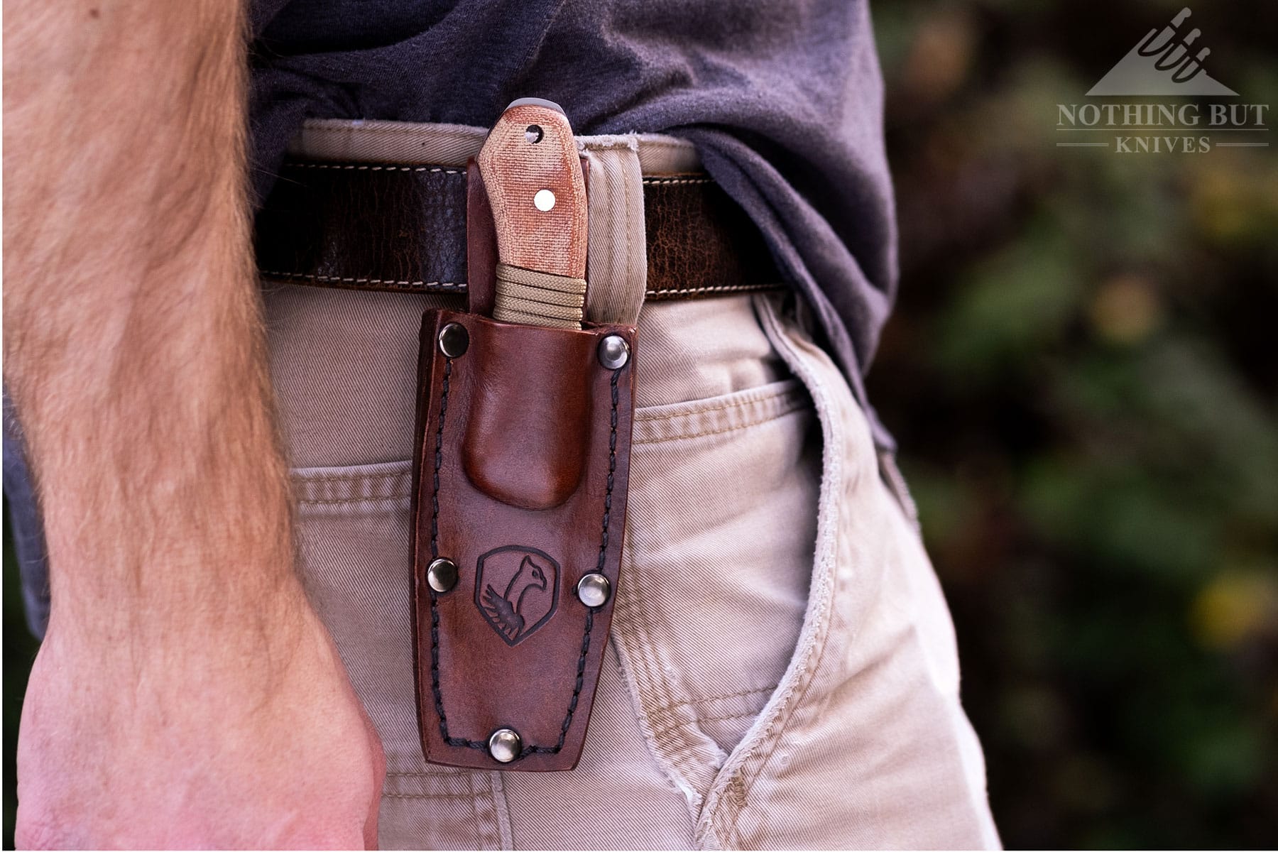 A close-up of the Condor Mountaineer Trail Wingman knife in its brown, leather sheath worn on a person's belt. 