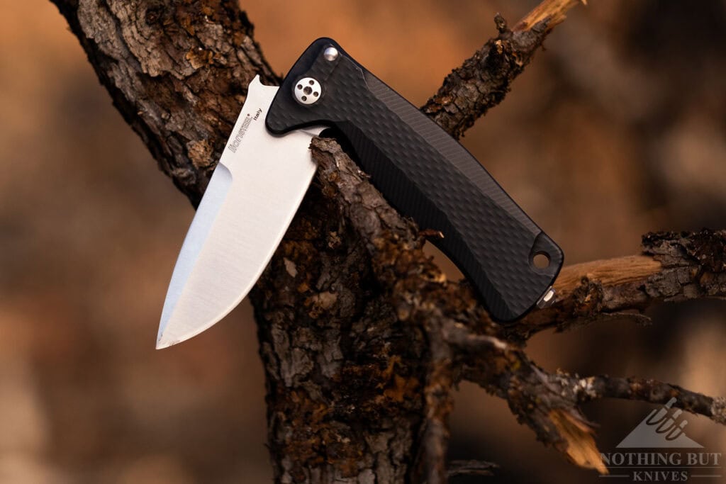 The LionSteel SR22 EDC knife shown here with the blade in the half open position resting on a small tree branch in the woods.