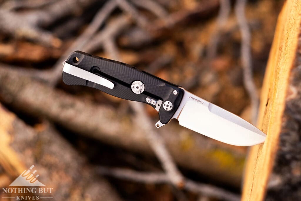 An overhead shot of the LionSteel SR22 with its blade sticking out of a tree limb and the right side of the knife handle facing the camera.