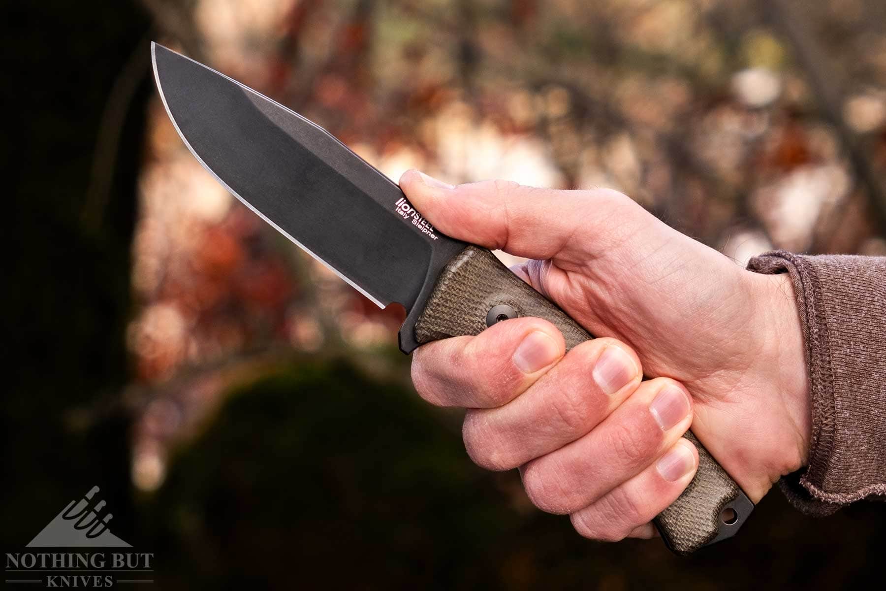 A close-up of the LionSteel M5 being gripped in a person's right hand in front of a background of forest foliage. 