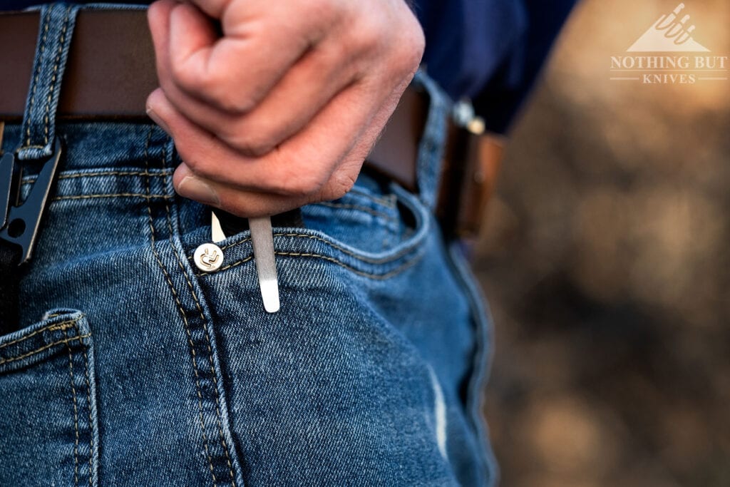 A close-up of a person's hand removing the LionSteel SR22 EDC knife from their right, front pants pocket.