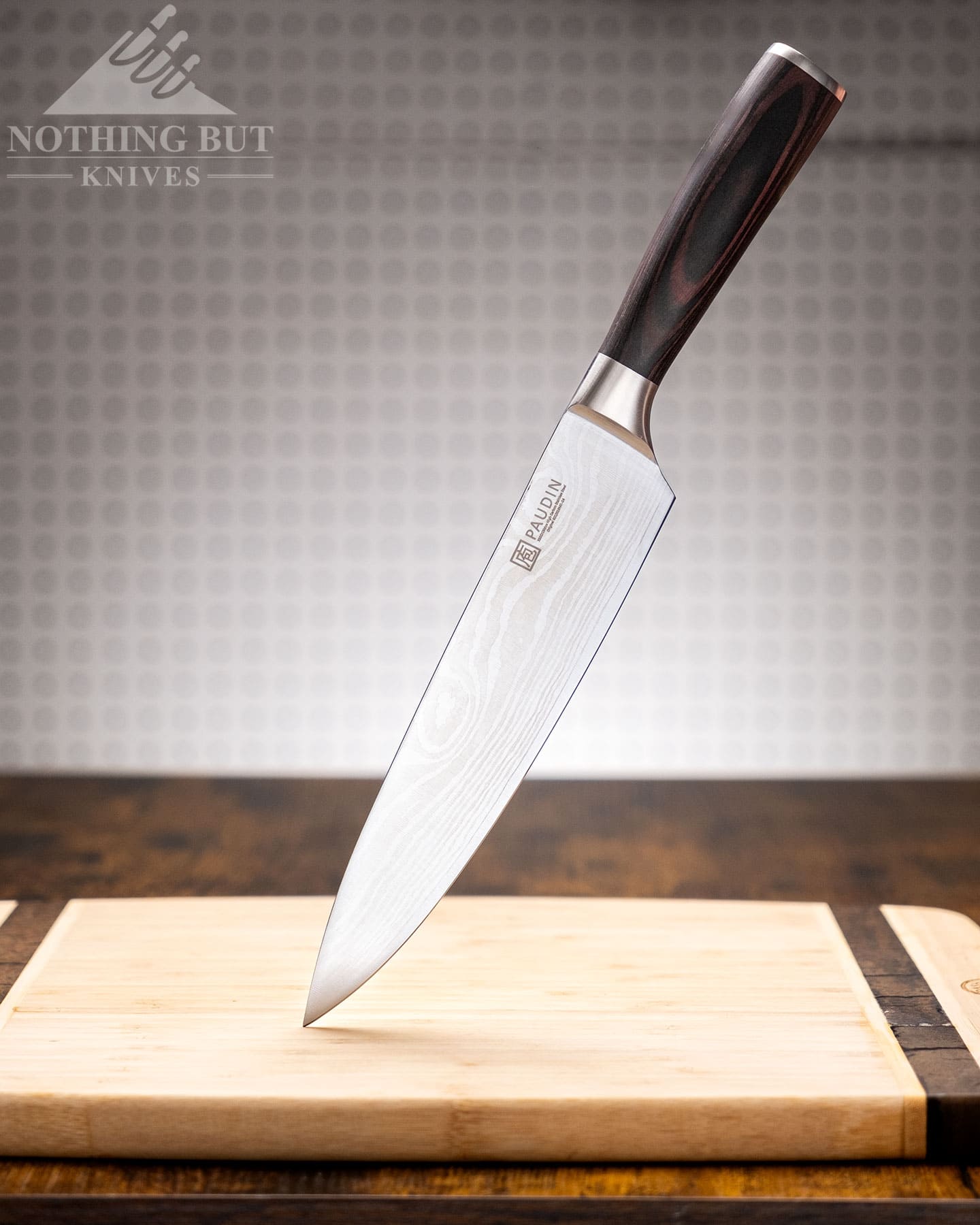 The Paudin chef knife standing on its blade tip on top of a Bamboo wood cutting board. 