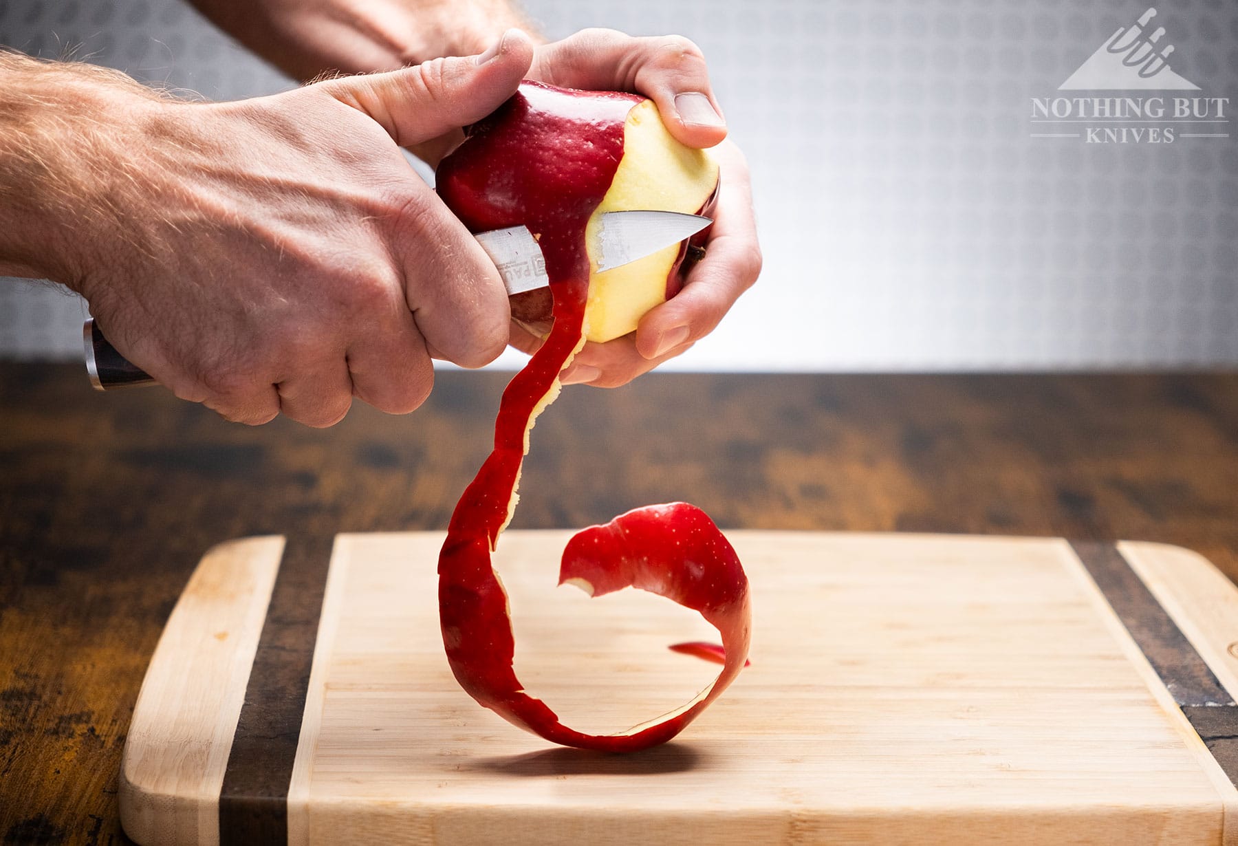 The Pauding Universal Collection paring knife being used to peel a red apple above a Bamboo wood cutting board. 