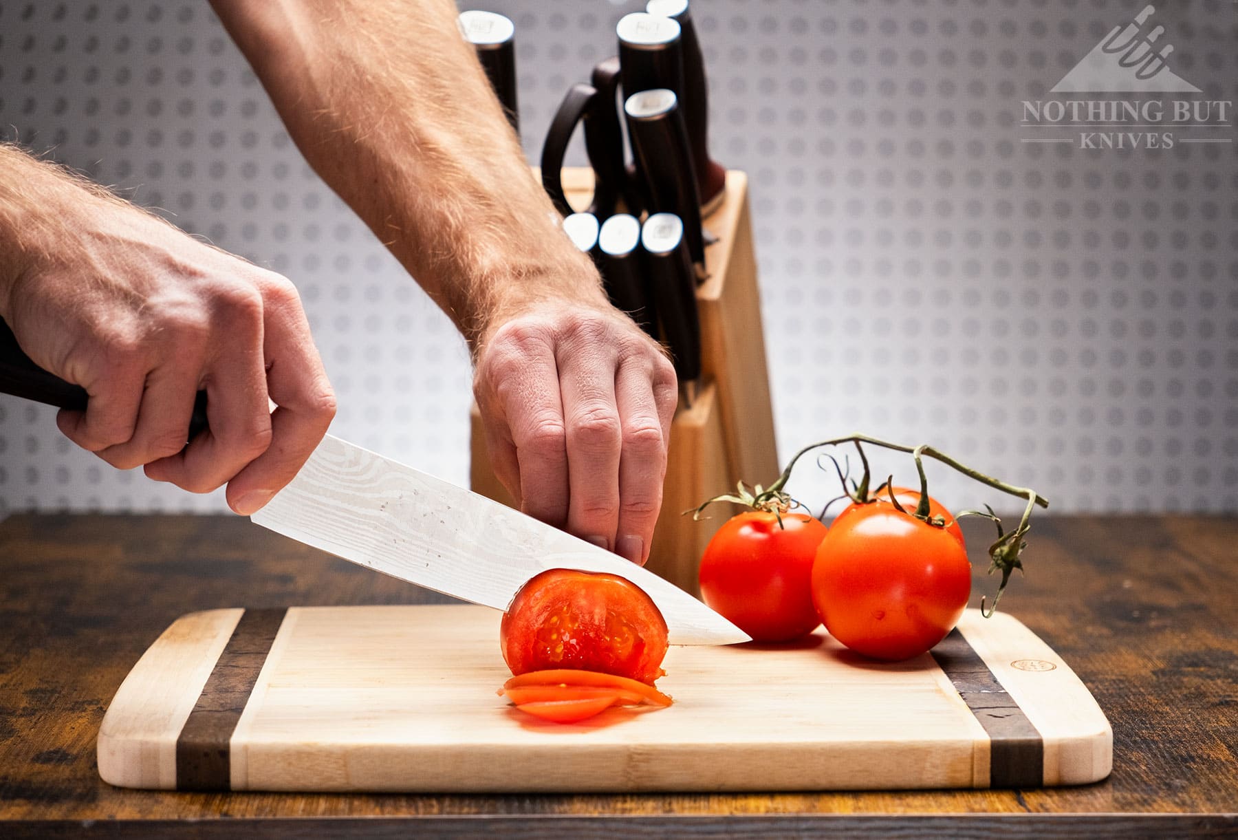 The Pauding 8 inch Universal Collection chef knife being used to slice a tomato on a Bamboo cutting board.