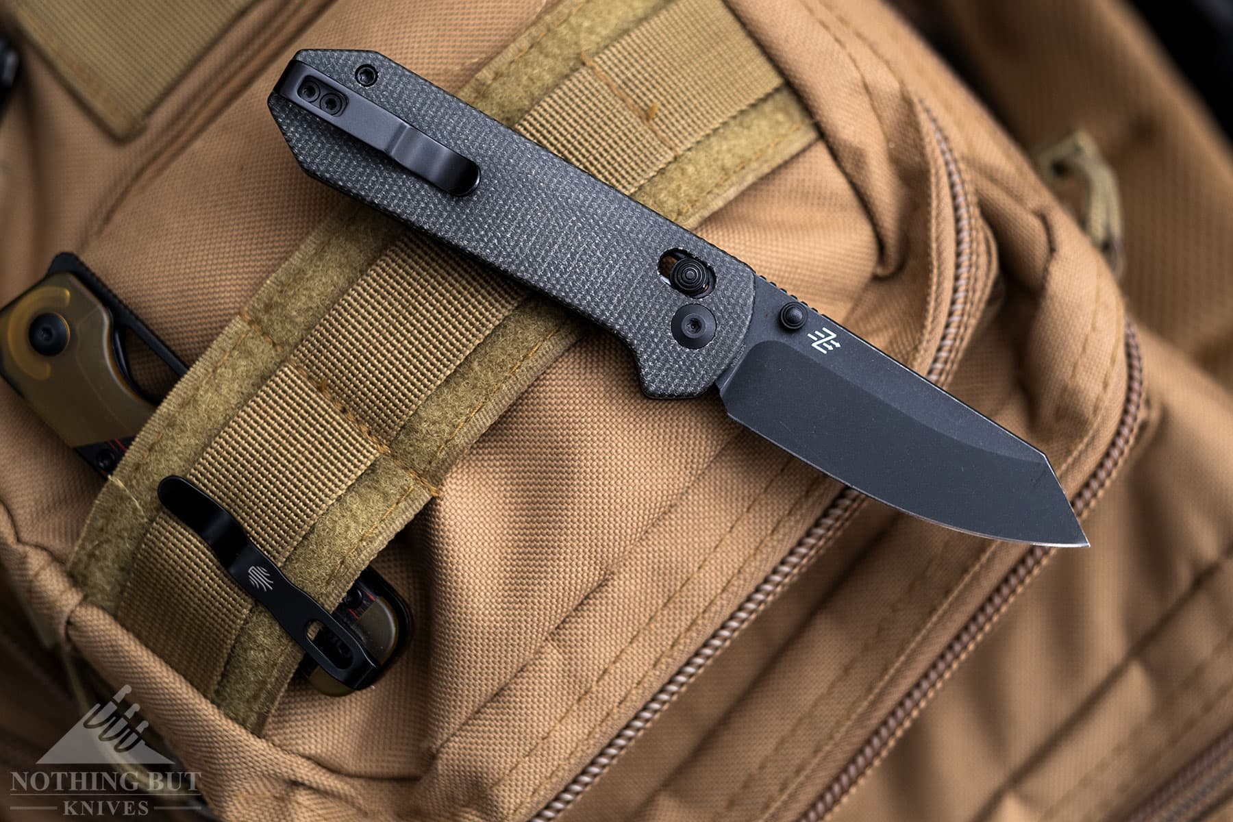 The Civivi Yonder folding knife shown here on top of a backpack next to the Kizer Militaw Mini. 