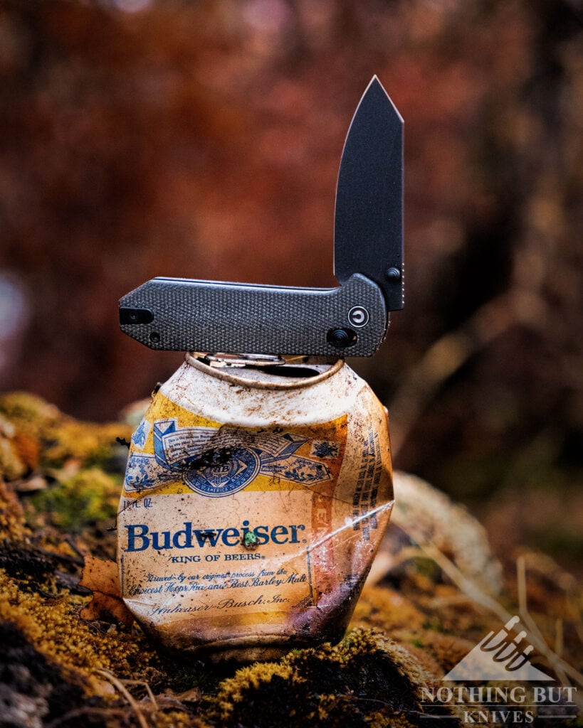 The Civivi Yonder EDC knife with its blade in the half open position sitting on a crushed vintage beer can.