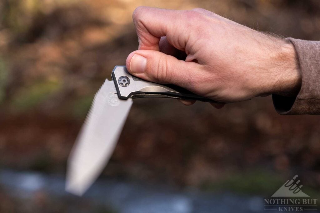 A close-up of the Off-Grid Scorpion folding knife being flipped open in front of a creek in a forest. 