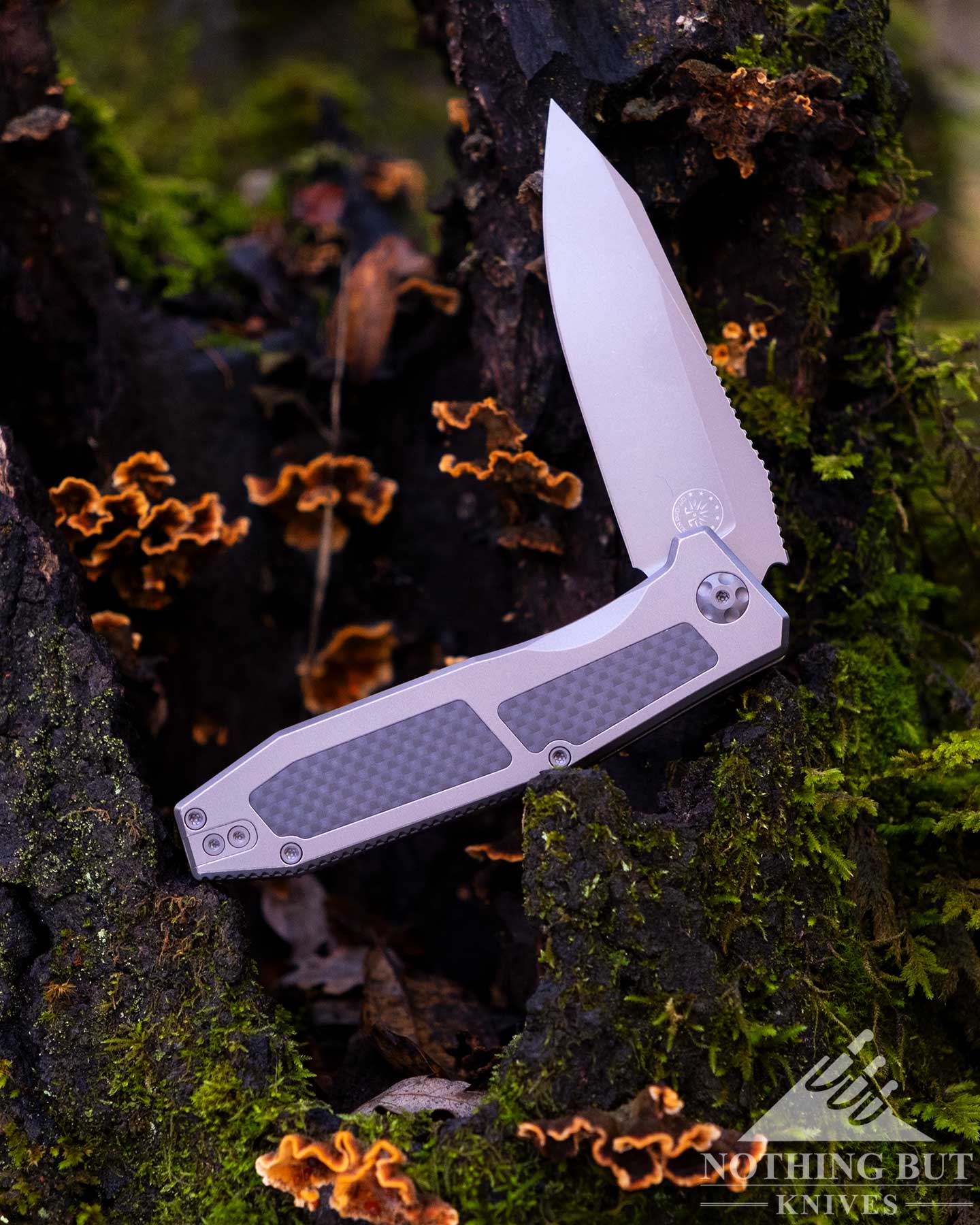 The Graywash version of the Scorpion V3 with its blade in the half open position balanced on a moss-covered tree stump. 