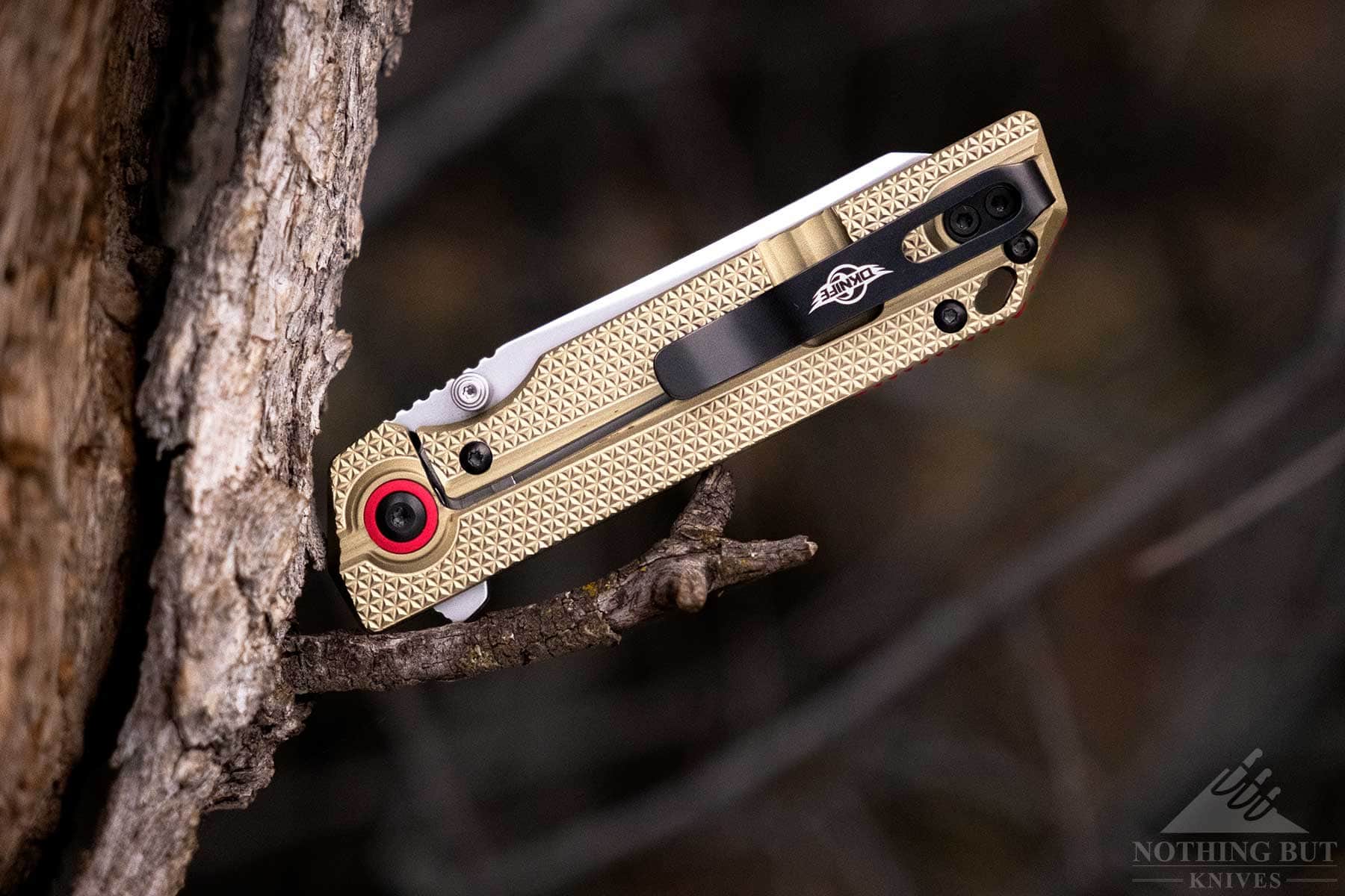 The Oknife XEN-OAL EDC pocket knife with its blade in the blosed position balanced on a small tree branch.