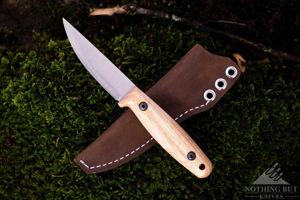 An overhead view of the BPS Finn Lite fixed blade knife crossed over its leather sheath on top of a moss-covered rock.