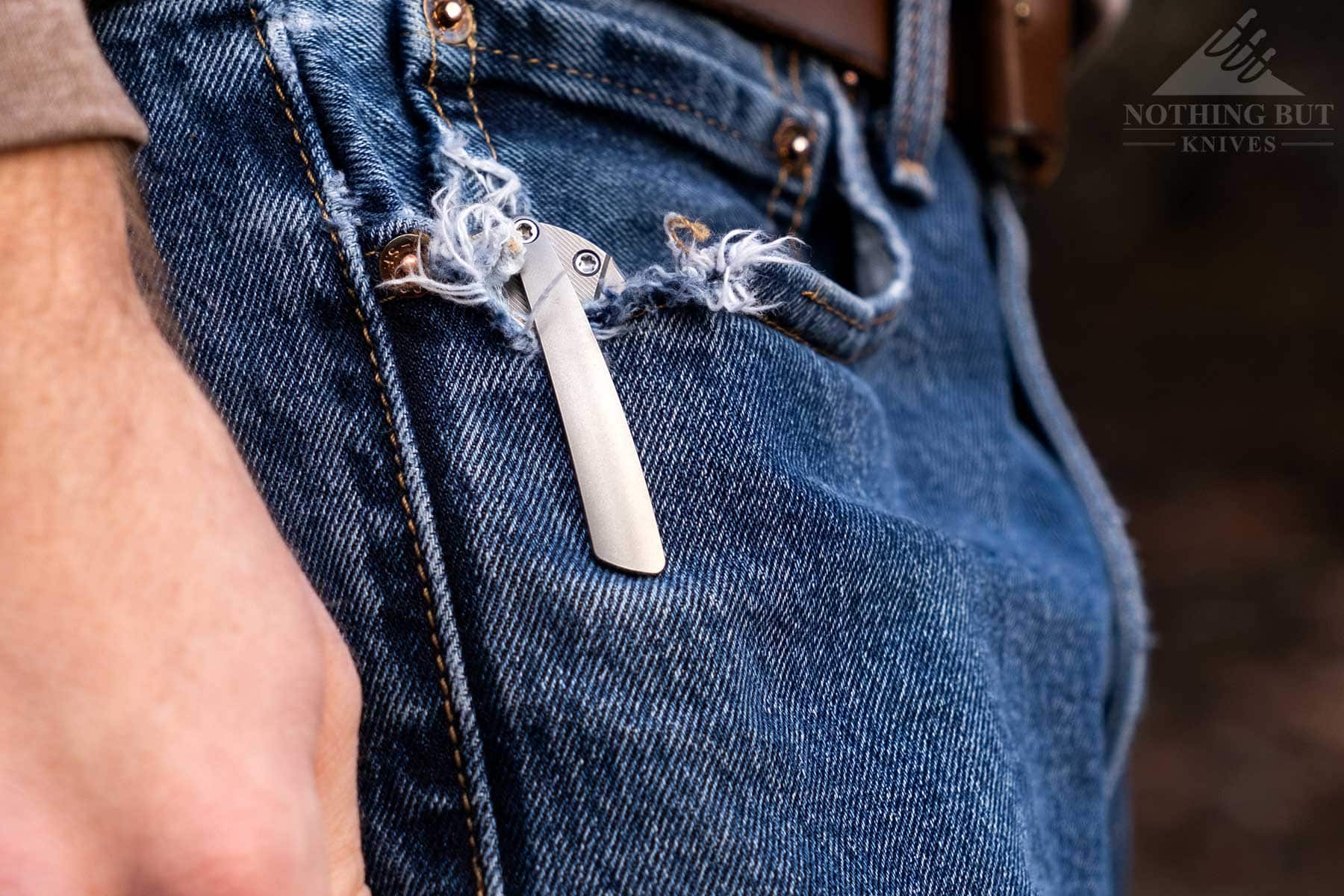 A close-up of the Kizer Hawk pocket clip attached to the frayed pocket of a person's jeans. 