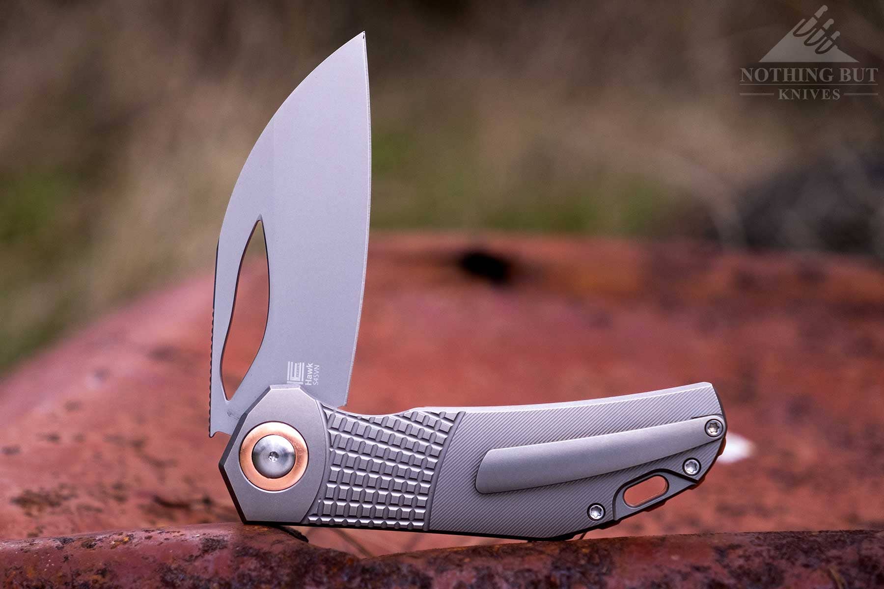 The Kizer Hawk liner lock folding knife shown here in the half open position on top of a rusty piece of metal. 