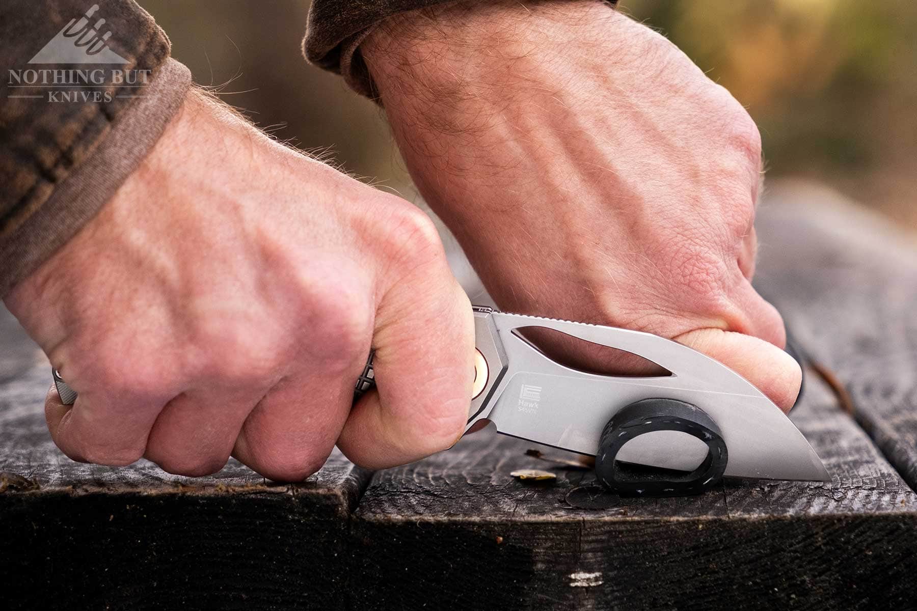 The blade of the Kizer Hawk slicing through rubber tubing on top of a picnic table outdoors. 