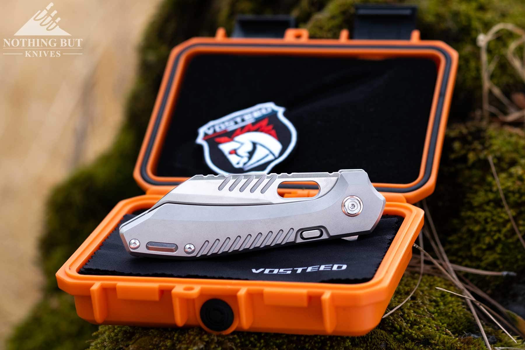 The Vosteed RSKAOS titanium pocket knife in the closed position on top of its orange case. 