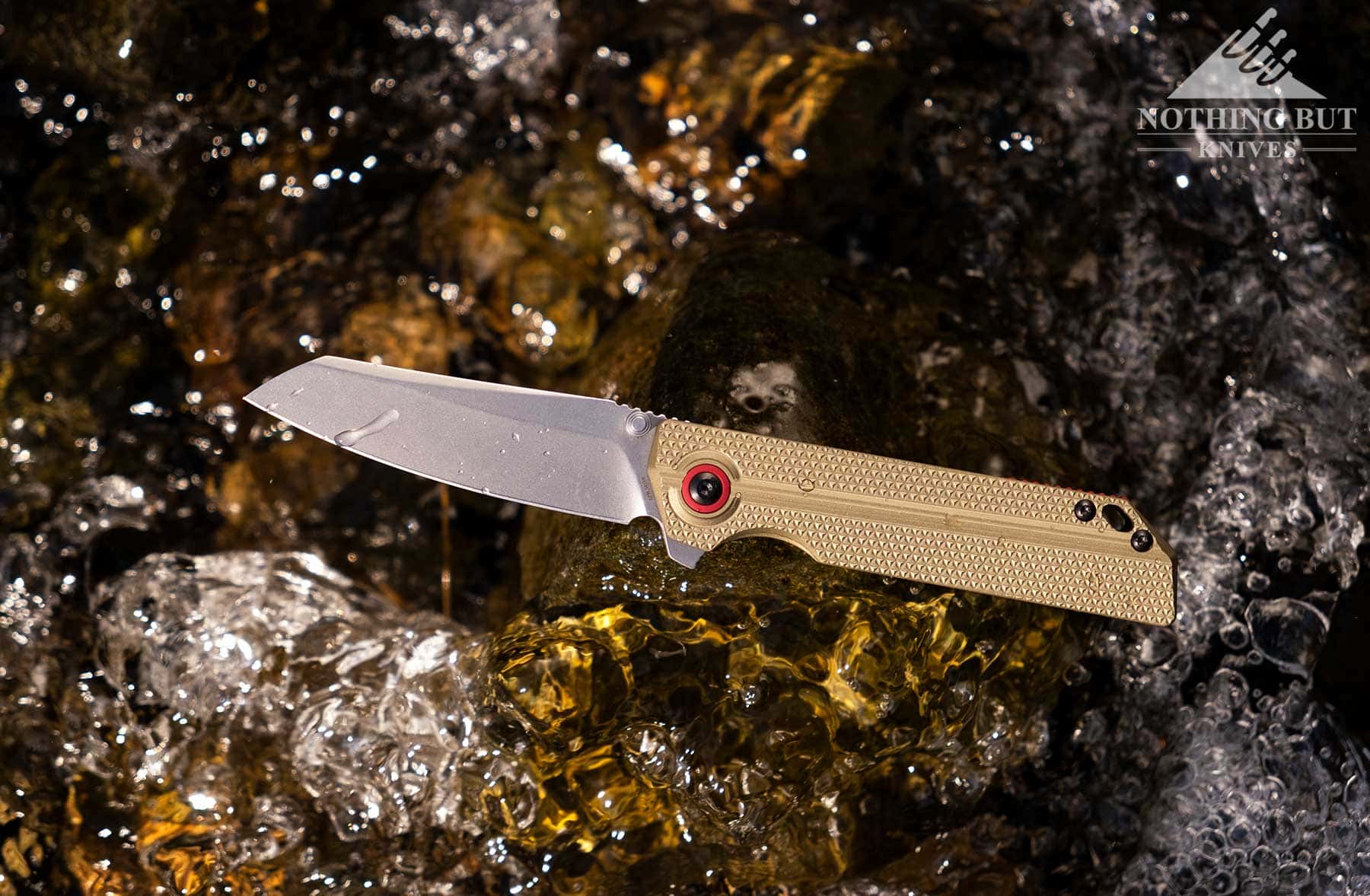 An overhead view of the Oknife XEN-OAL pocket knife with the S45VN steel blade in the open position on a log above a creek. 