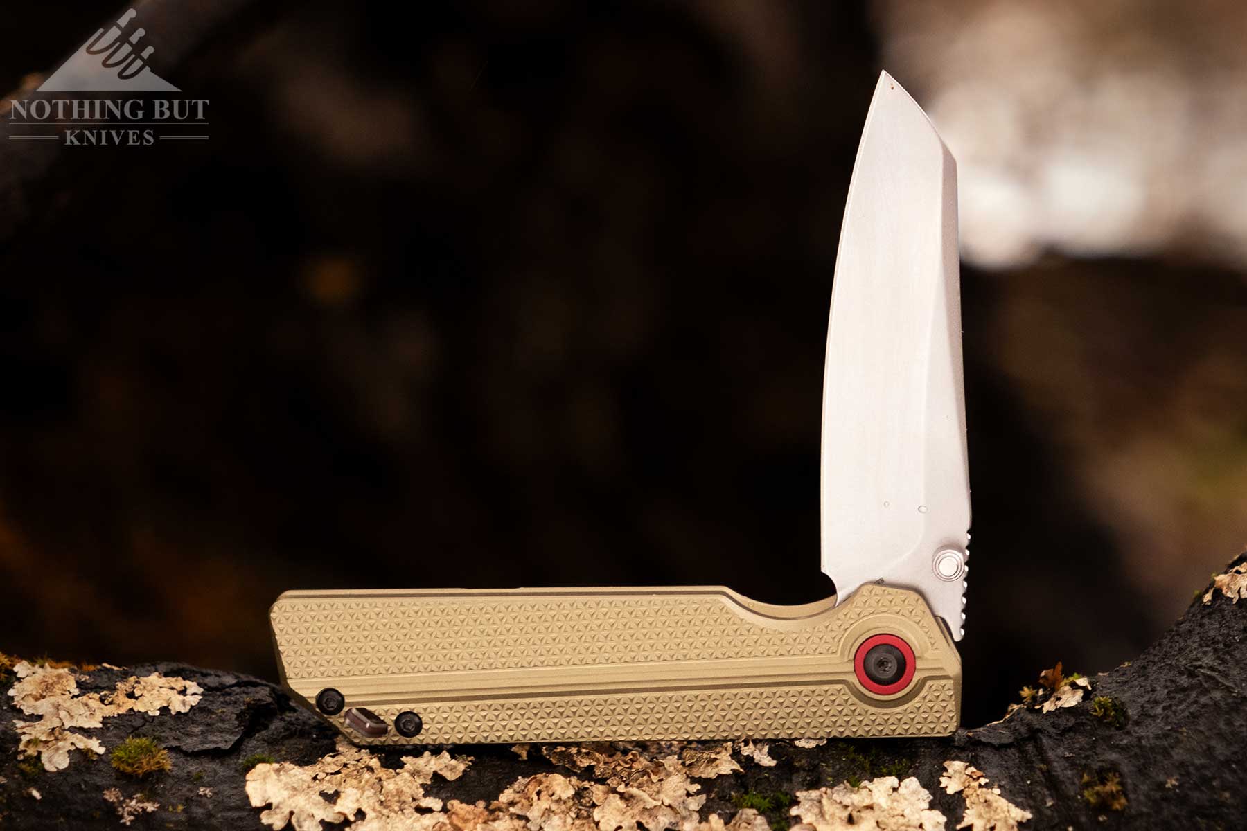 A close-upof the XEN-OAL pocket knife in the half open position resting on a moss-covered rock outdoors. 