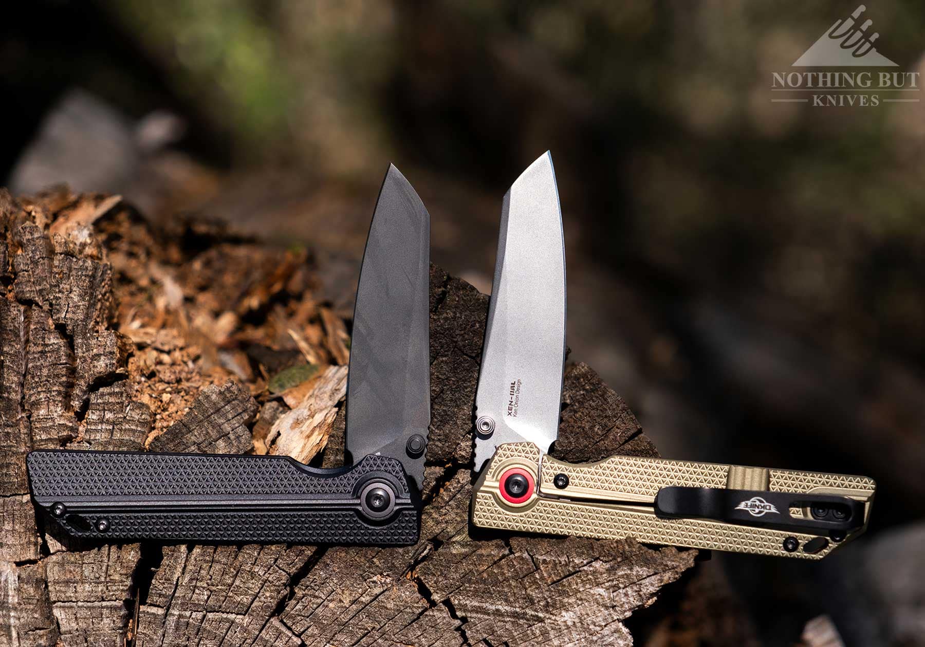 The matte black and olive green models of the Oknife XEN-OAL EDC knife in the half open position on a log. 