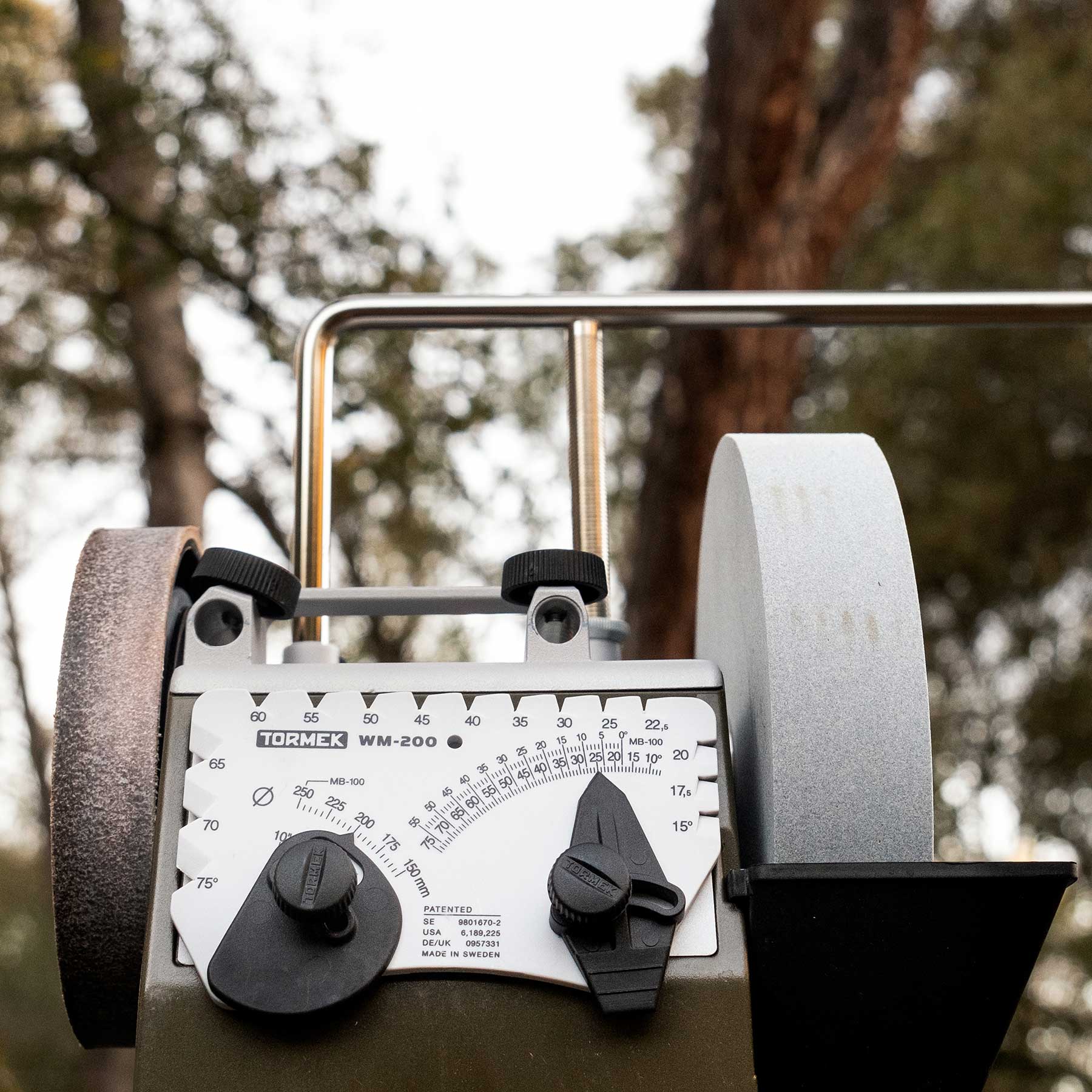 A front view shot of the Tormek T-4 Bushcraft knife sharpener outside with trees and the sky in the background.