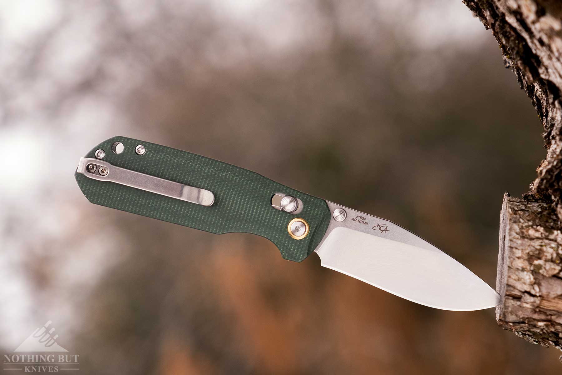 A folding knife with green Micarta scales sticking in a tree.