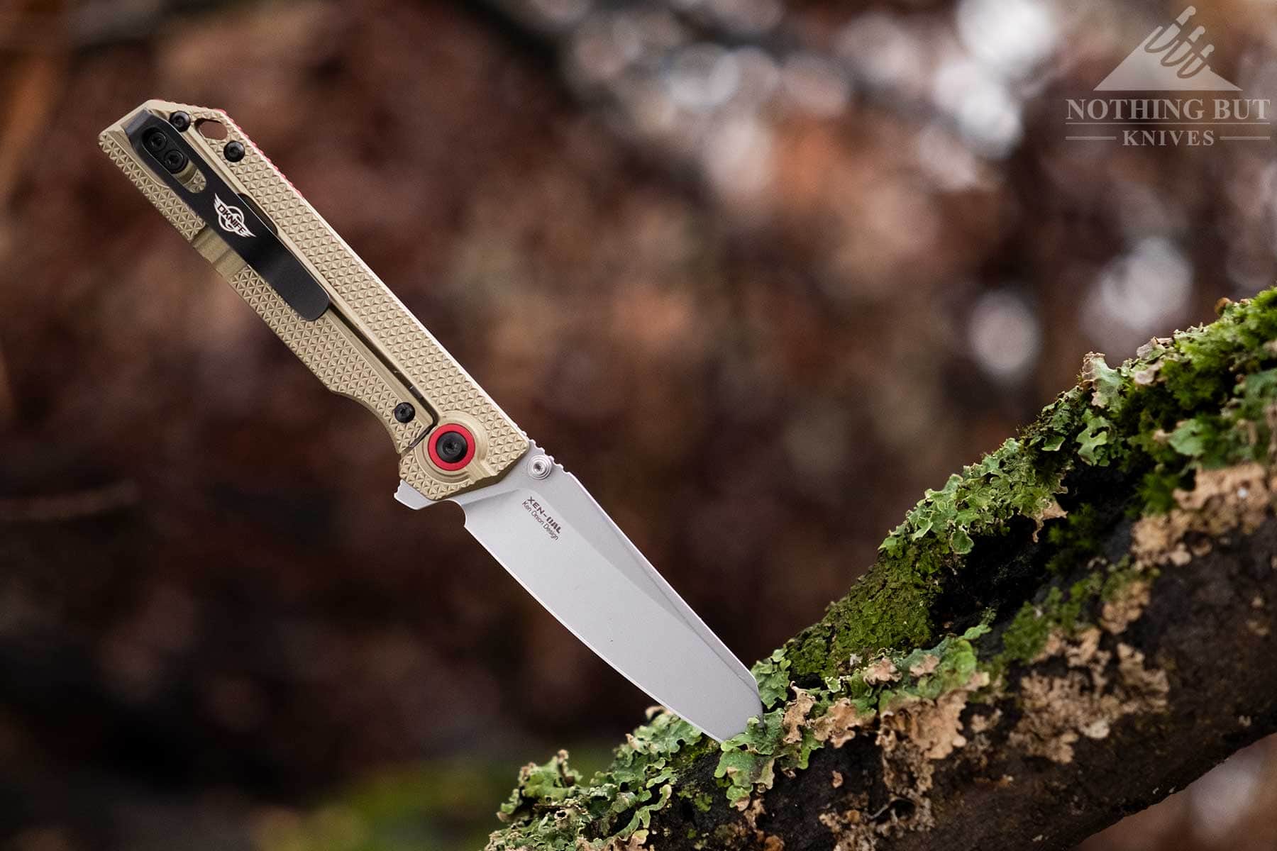 A side view of the XEN-OAL folding knife sticking out of a tree limb in the forest. 